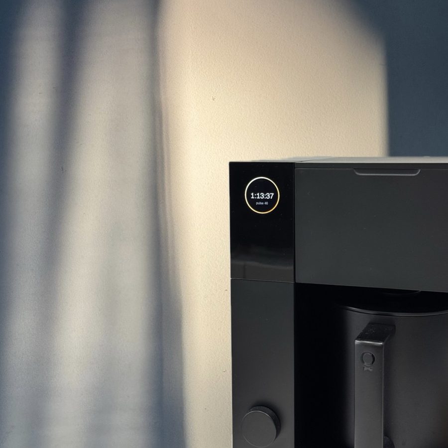 A precision brewer's round display showing a live shot timer against soft window light.