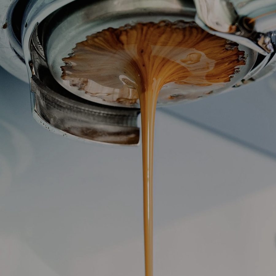 A honey-coloured espresso shot pulling from a bottomless portafilter in close-up.