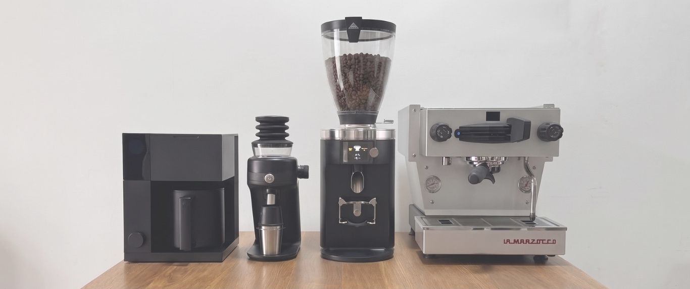 batchhouse's mobile coffee bar equipment — a batch brewer, two grinders and a La Marzocco espresso machine lined up on a timber counter against a pale wall.